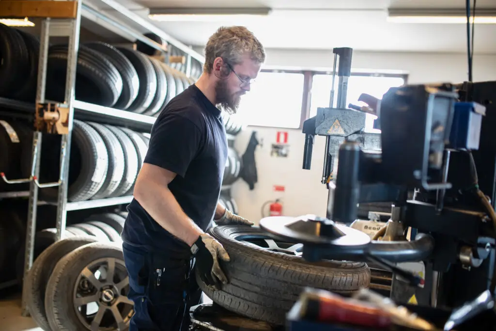 Mekaniker i en verkstad använder en maskin för att byta däck på en fälg.