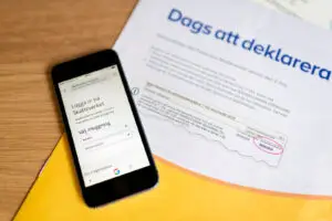 Deklarationspapper från Skatteverket med en mobiltelefon som visar inloggningssidan till Skatteverkets e-tjänster.